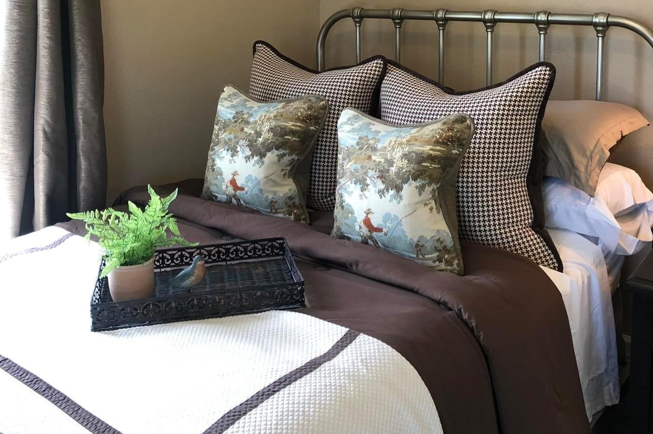 Decorative pillows on a bed with a plant and decorative tray.