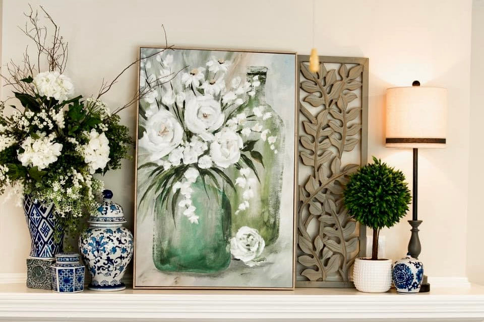 Decorative mantel with floral arrangement, framed artwork, and decorative items.