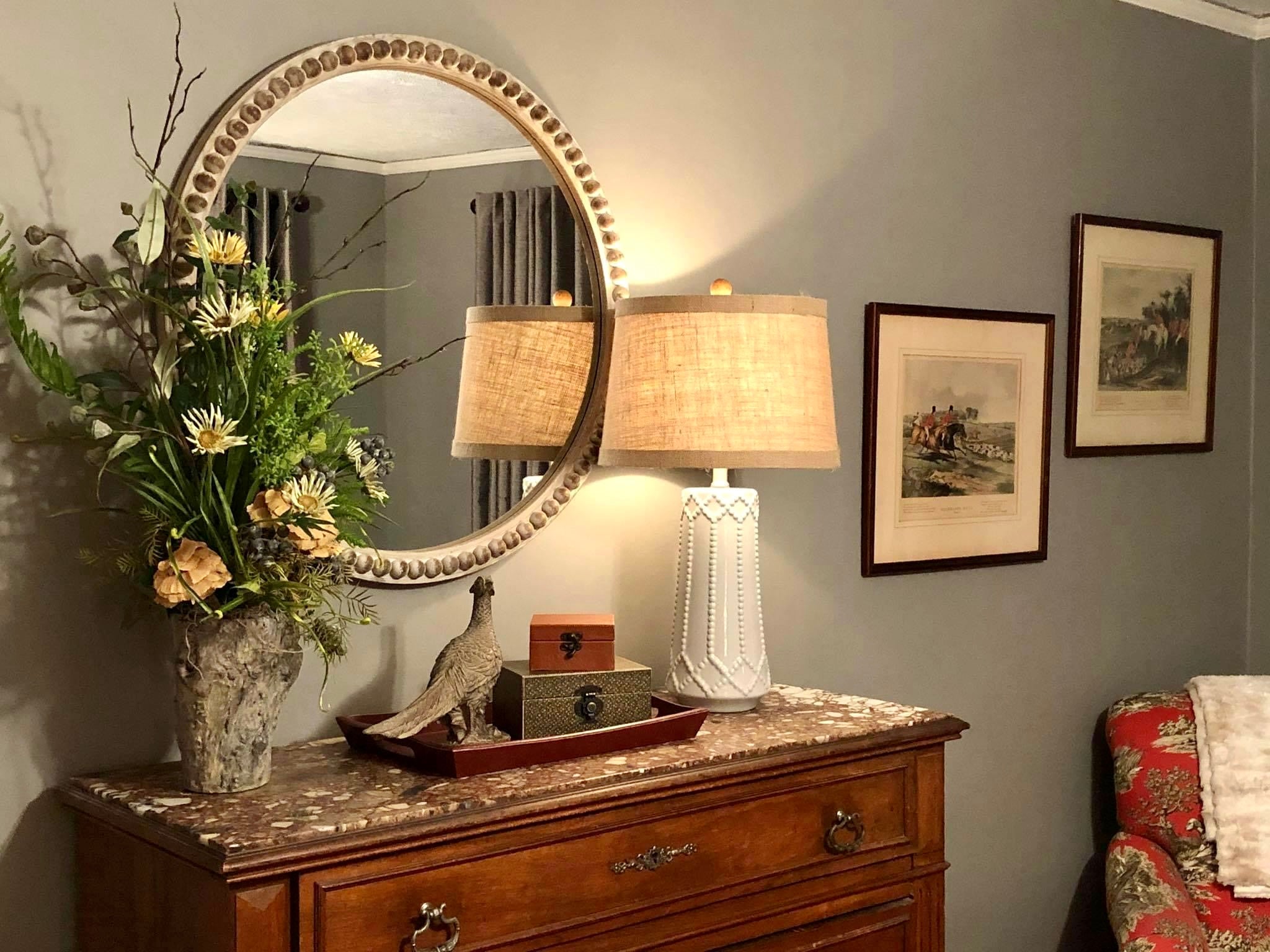Decorative room interior with a mirror, lamp, and framed pictures on a gray wall.