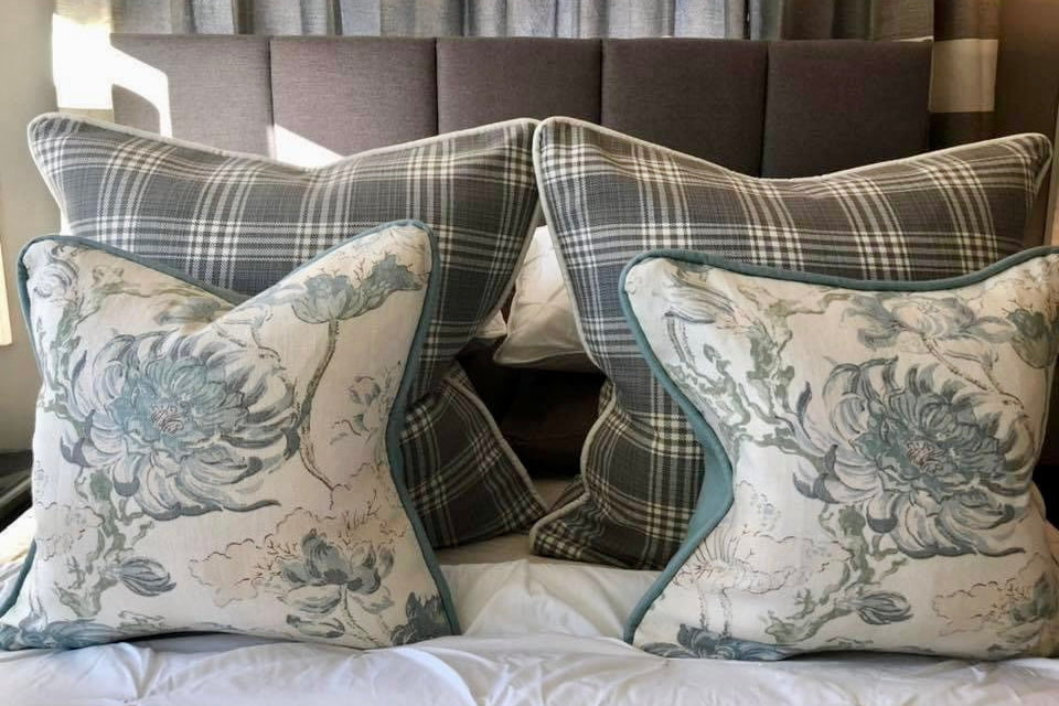 Decorative pillows with floral and plaid patterns on a bed.