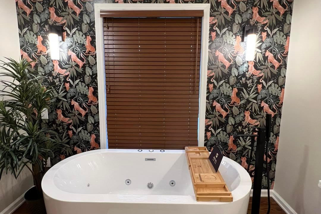 Bathroom with a white freestanding bathtub against a wall with floral wallpaper.