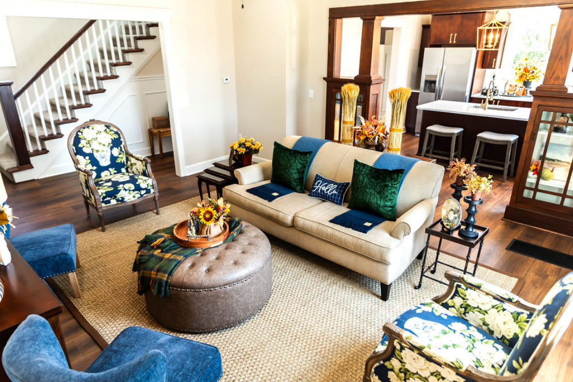 Perfectly styled living room with matching navy fabric accent chairs, an ottoman with a decorative tray, a fluffed sofa, and two ginger jar navy and green accent chairs. 