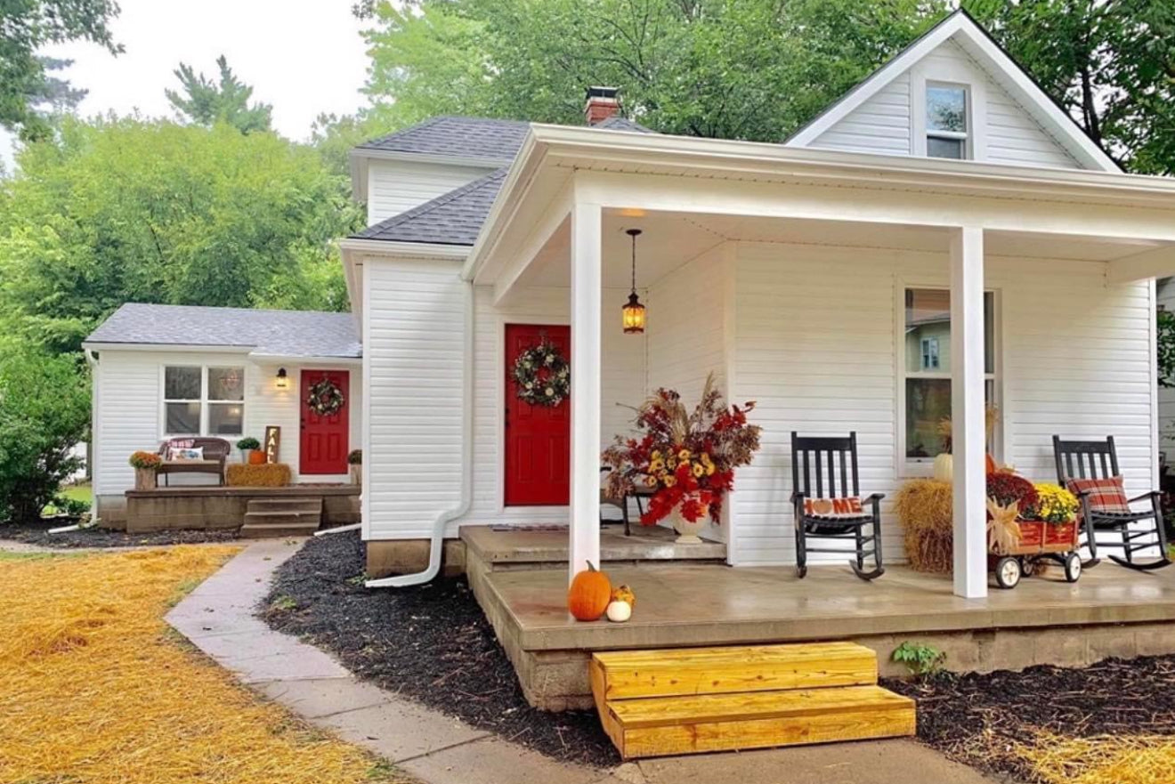 White house with a porch decorated for fall, featuring pumpkins and autumn-themed decor.