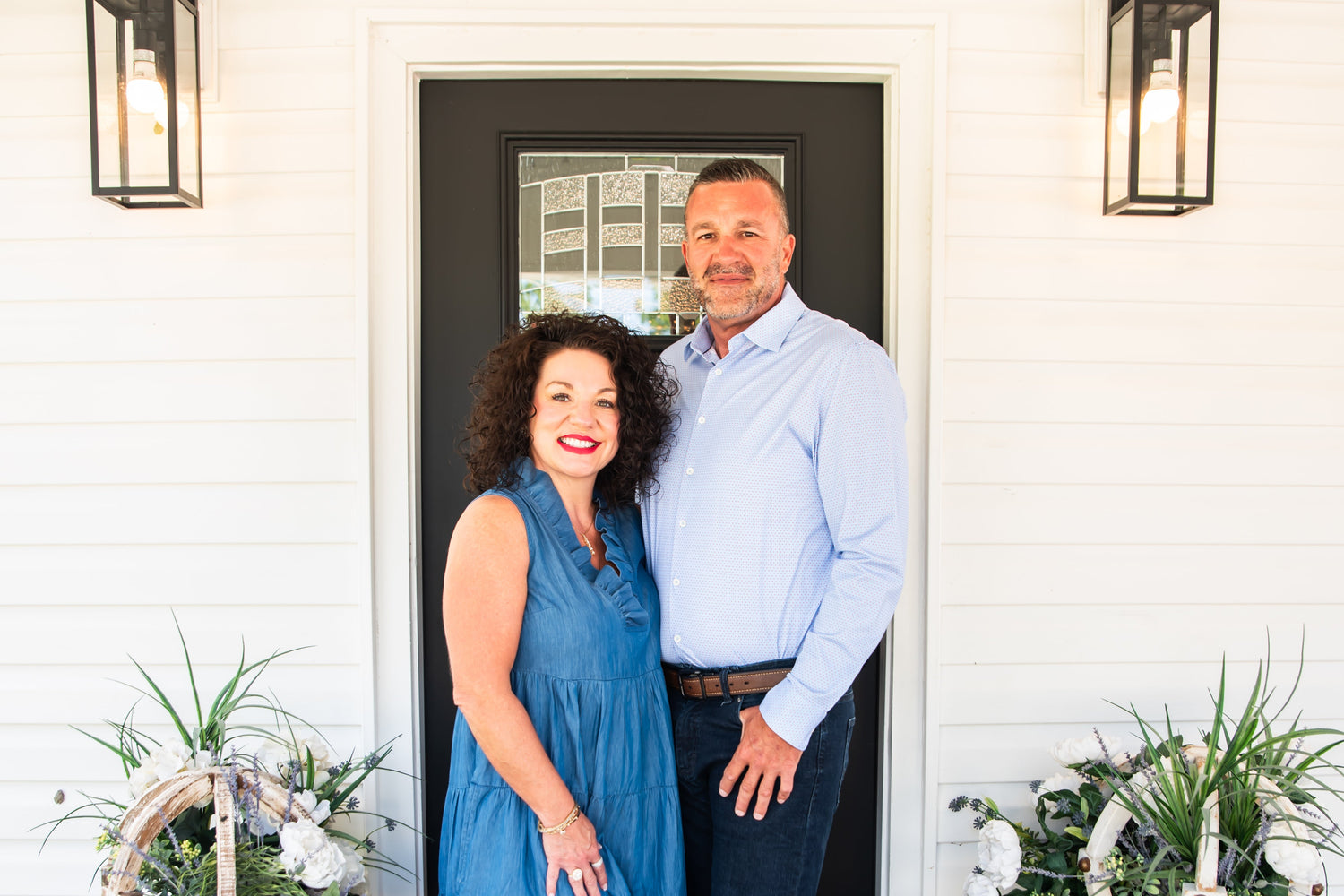 Man and woman standing on a porch with Halloween decorations, including pumpkins and a witch.