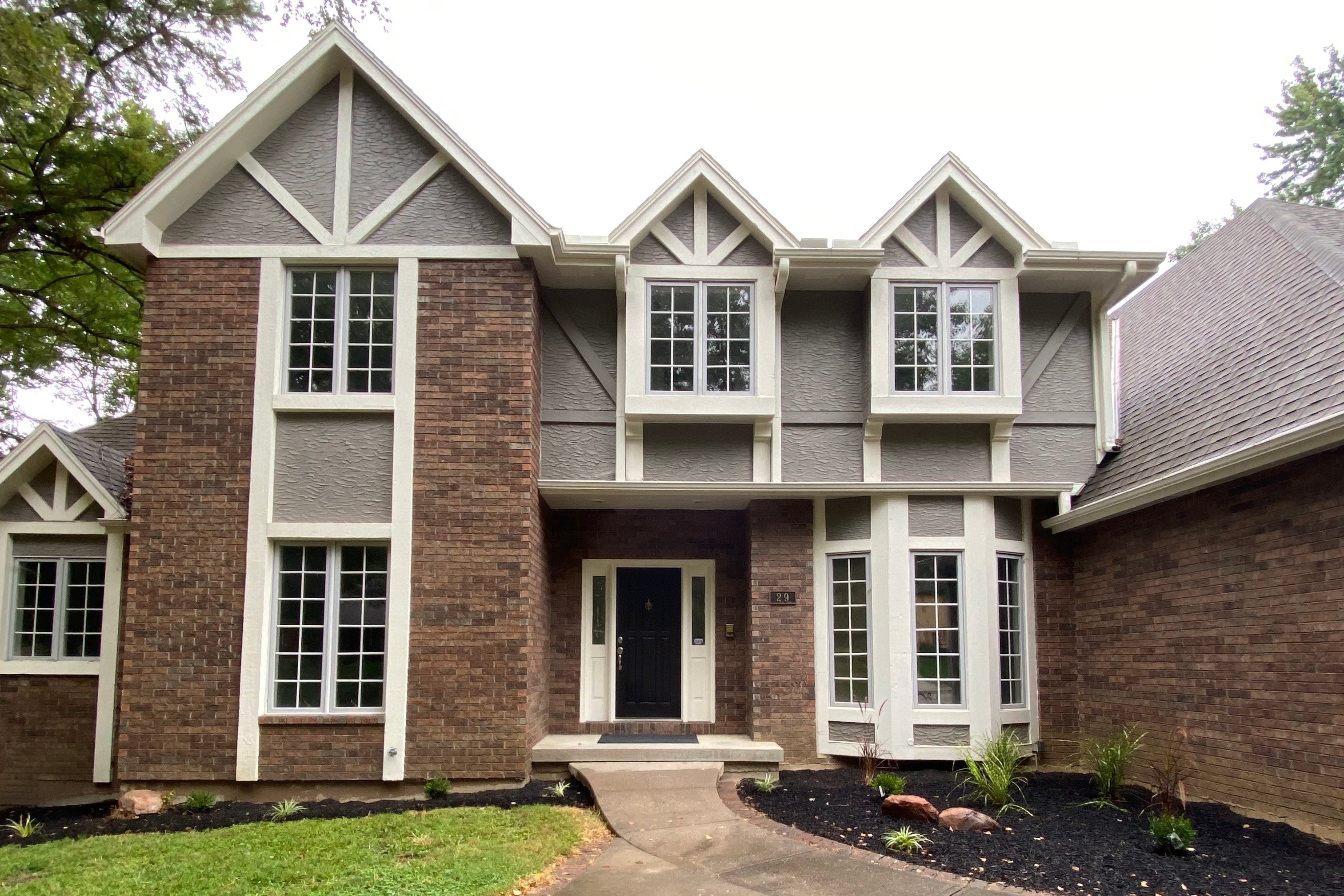 Two-story house with brick and siding exterior, driveway, and green lawn.