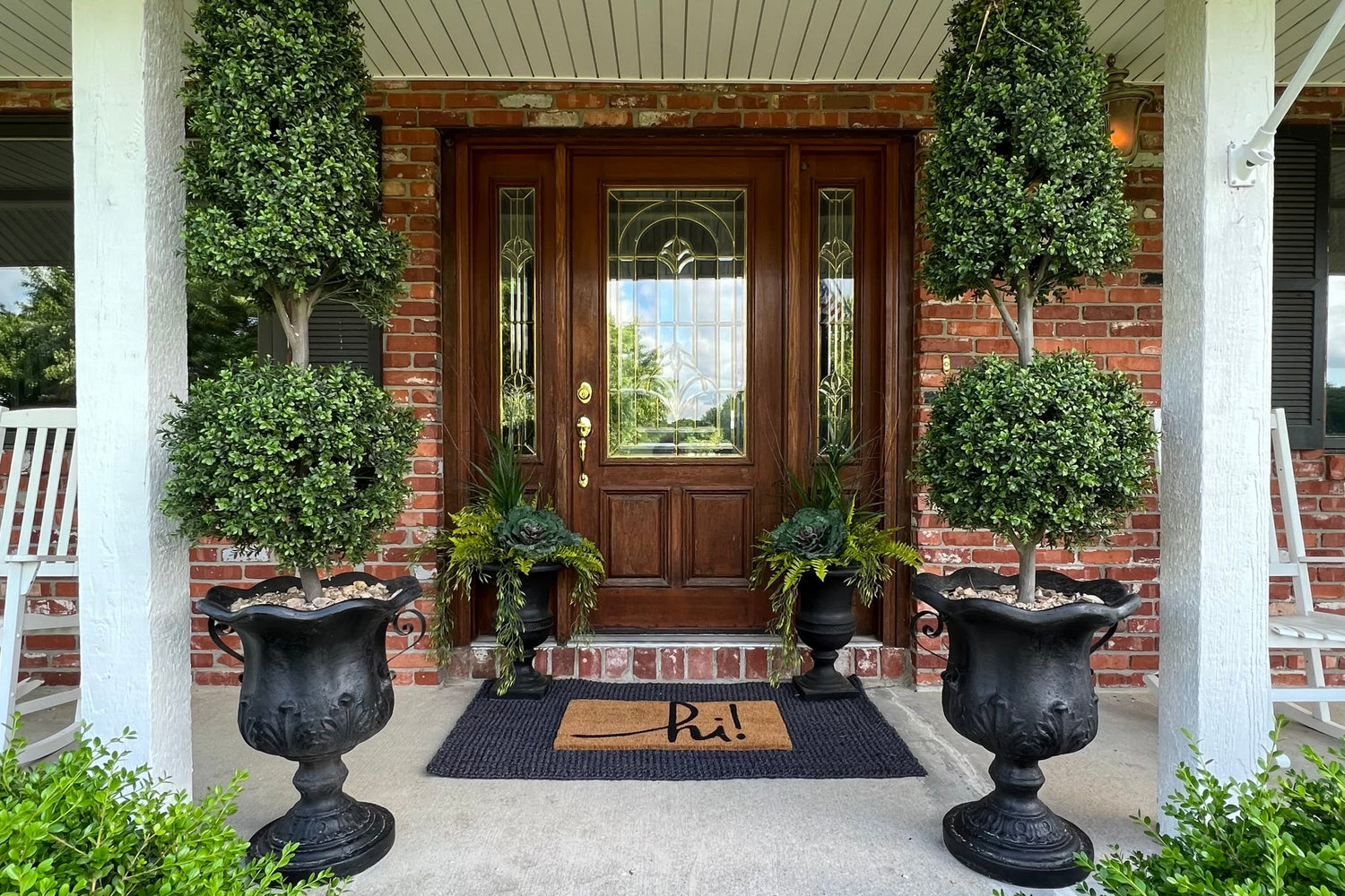 Front door with decorative plants and urns on a porch
