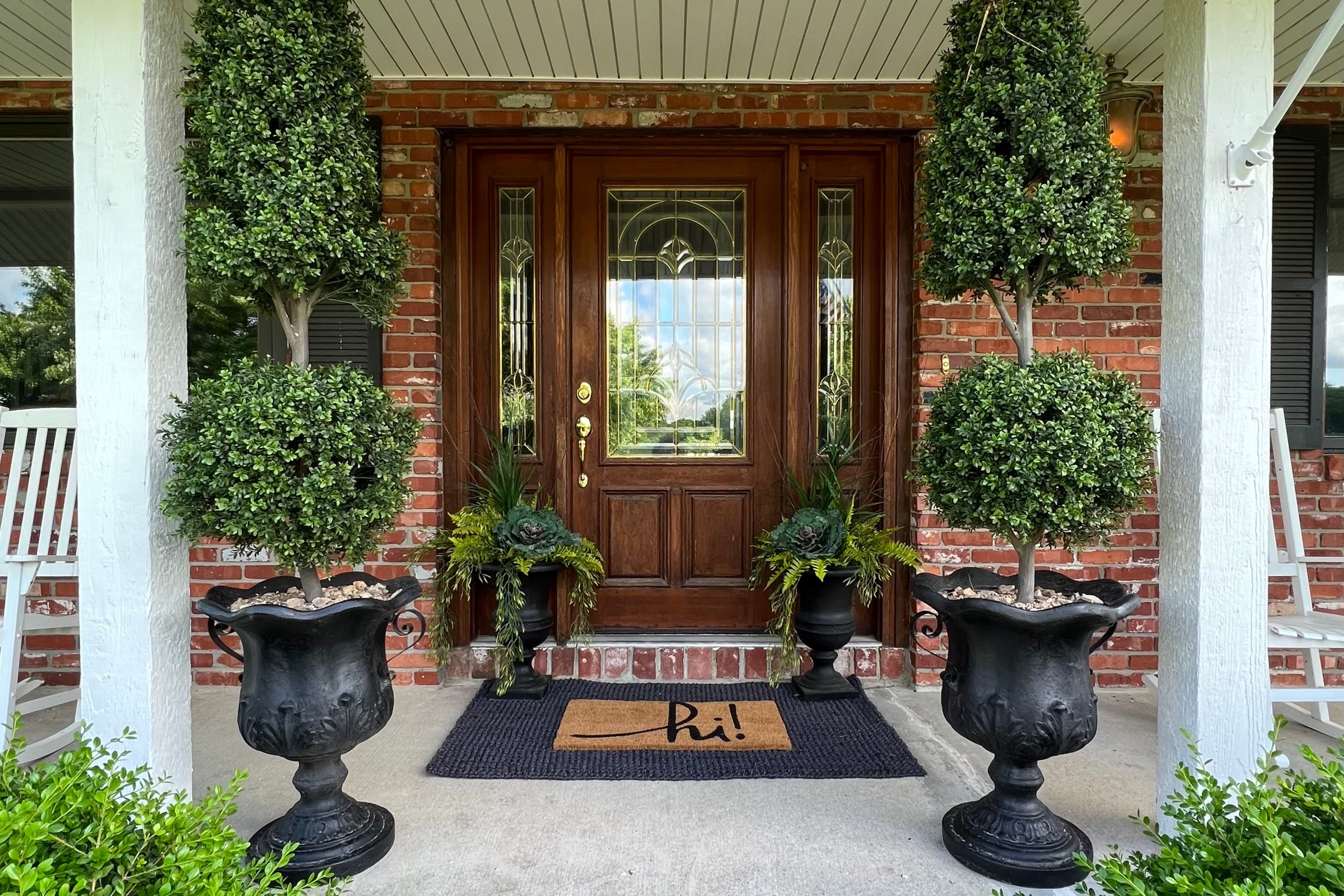 Front door with decorative plants and urns on a porch