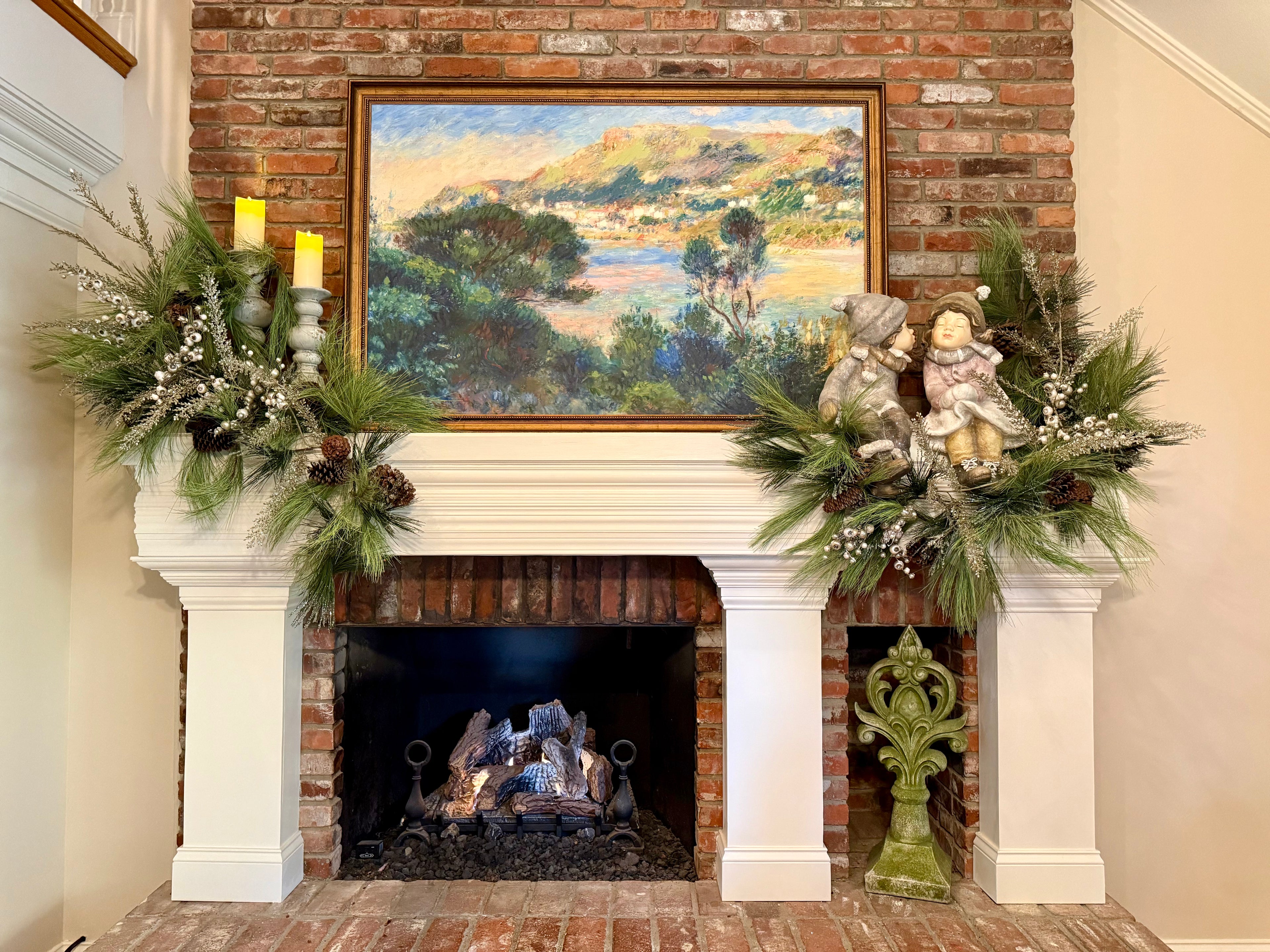 Beautifully decorated fireplace mantle with large artwork, boy and girl statues, and pine garlands. 