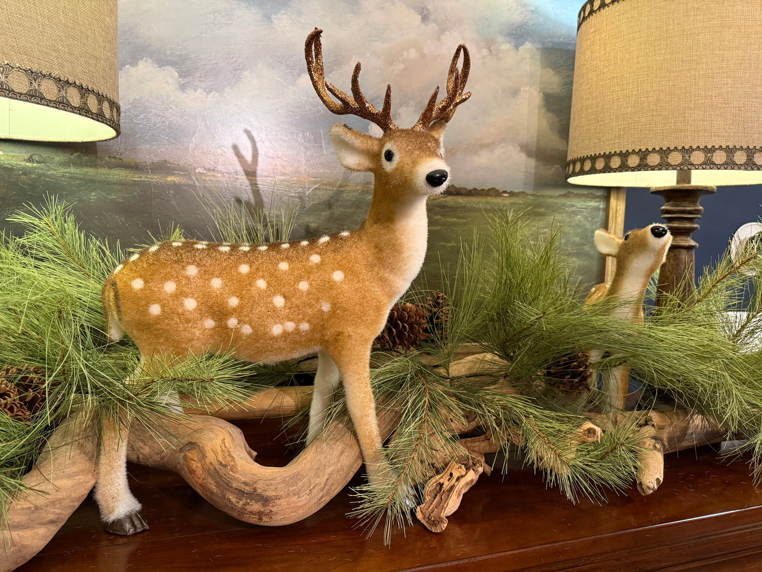 Faux deer and bear figurines on a decorative shelf with greenery and lamps in the background.