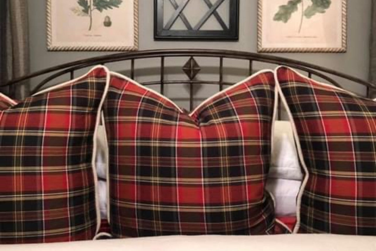 Plaid pillows on a bed with wall art and a mirror in the background.