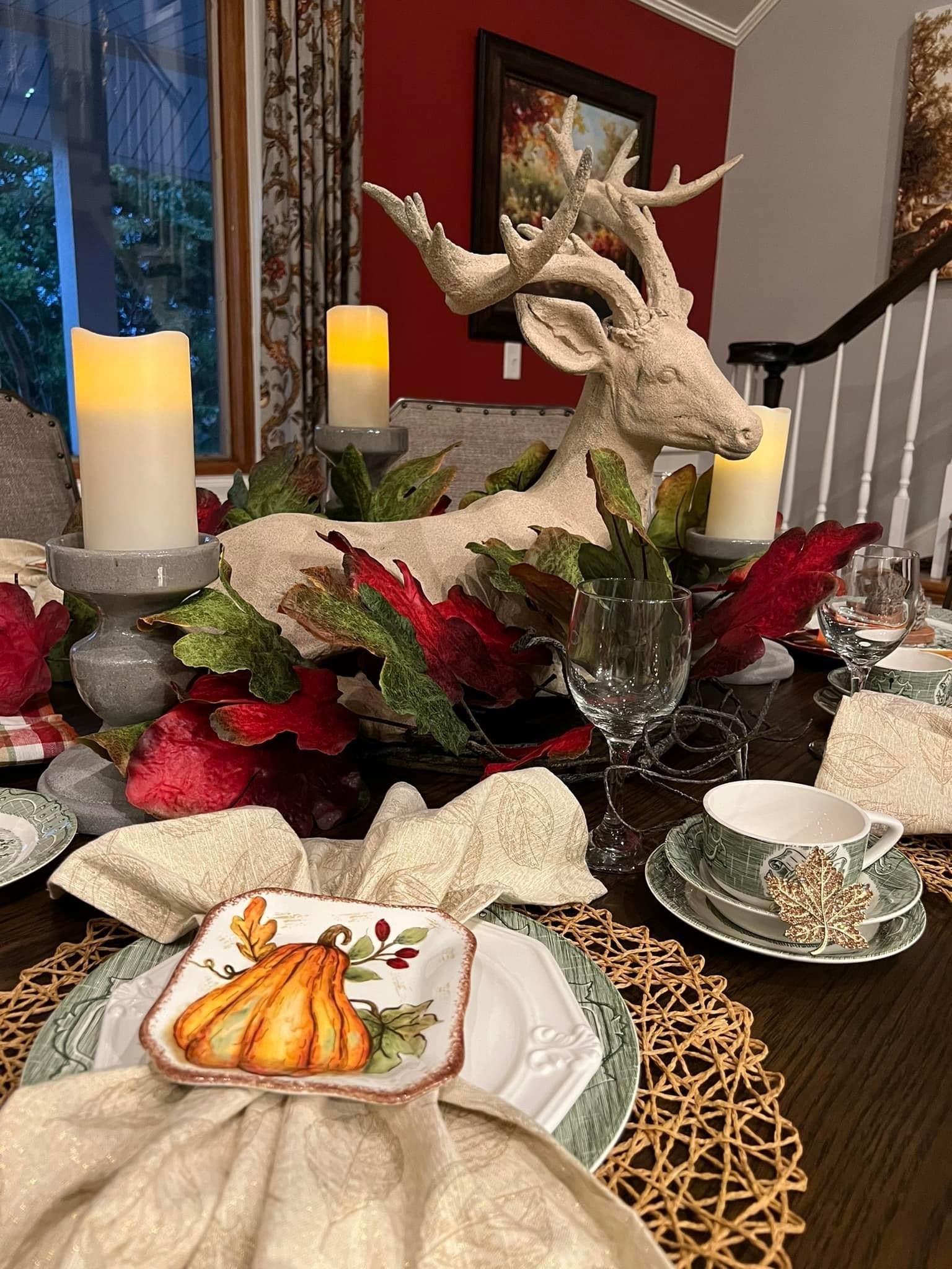 Decorated dining table with fall-themed centerpieces, candles, and a deer head sculpture.