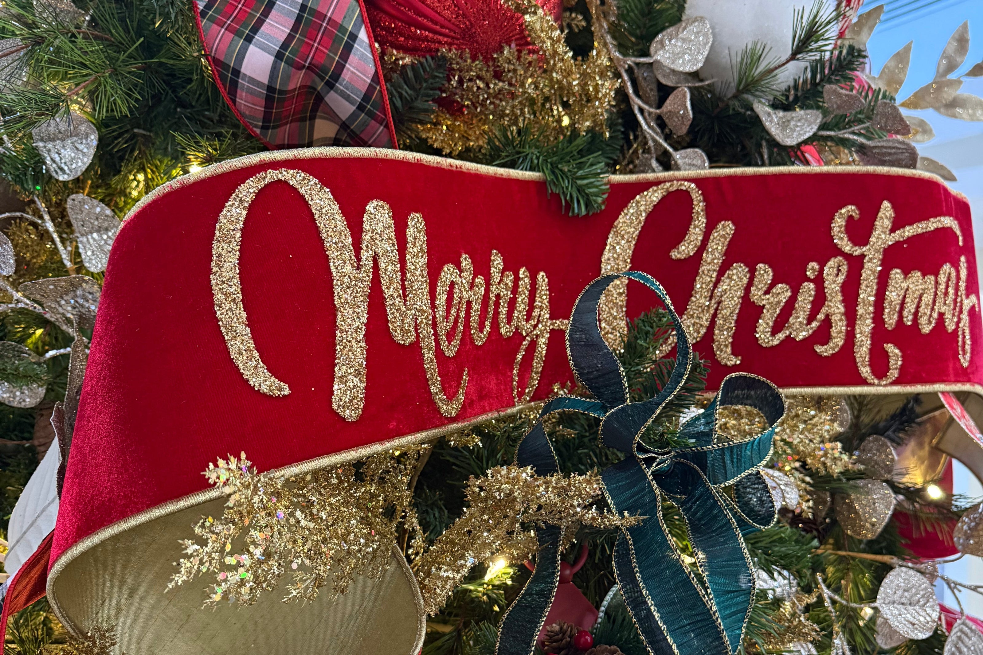 Merry Christmas banner ribbon on an elegant Christmas tree decorated with traditional colors, plaids, crystal snowflakes, lanterns, and glistening garlands. 