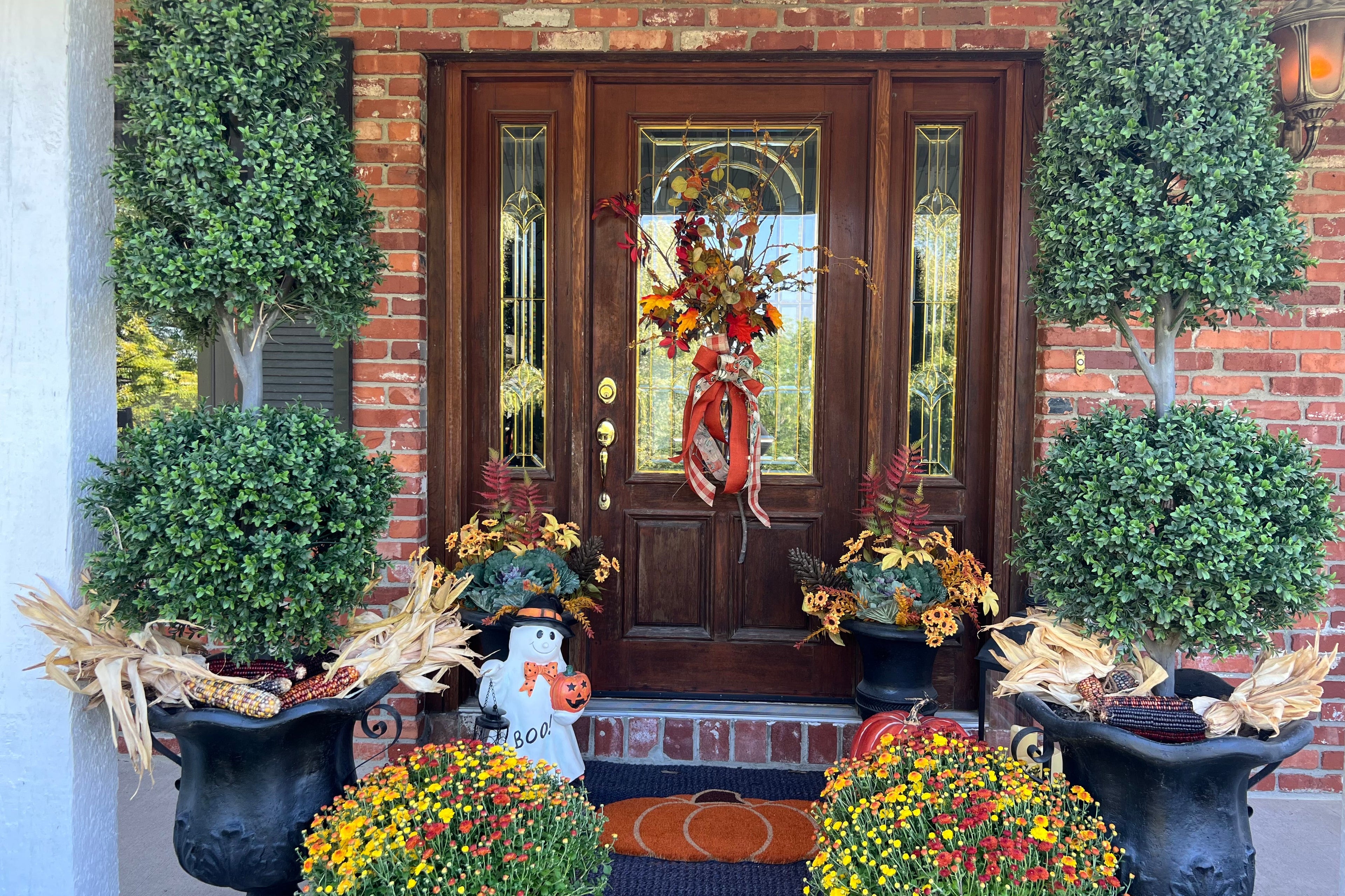 Decorative front door with wreath, potted plants, and fall-themed decorations on a brick house.