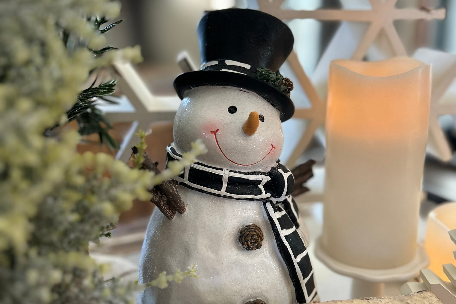 Decorative snowman with a black top hat and scarf, surrounded by winter elements like a candle and branches.