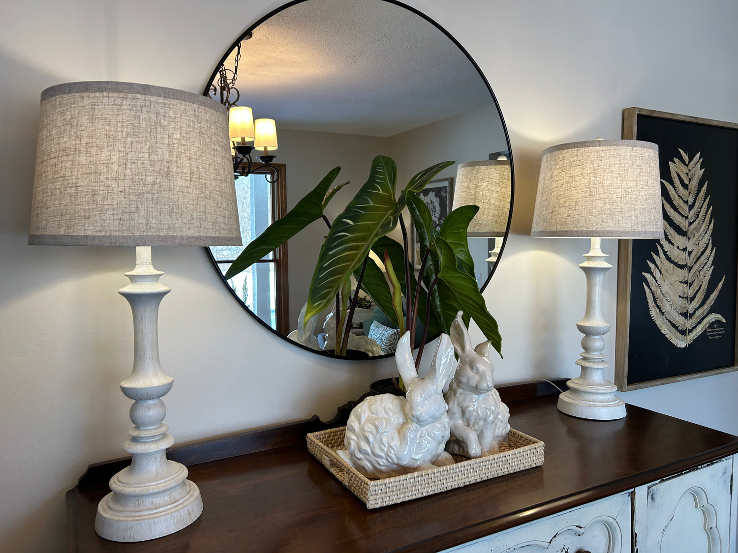 Decorative table with lamps, a mirror, and decorative items in a room setting.