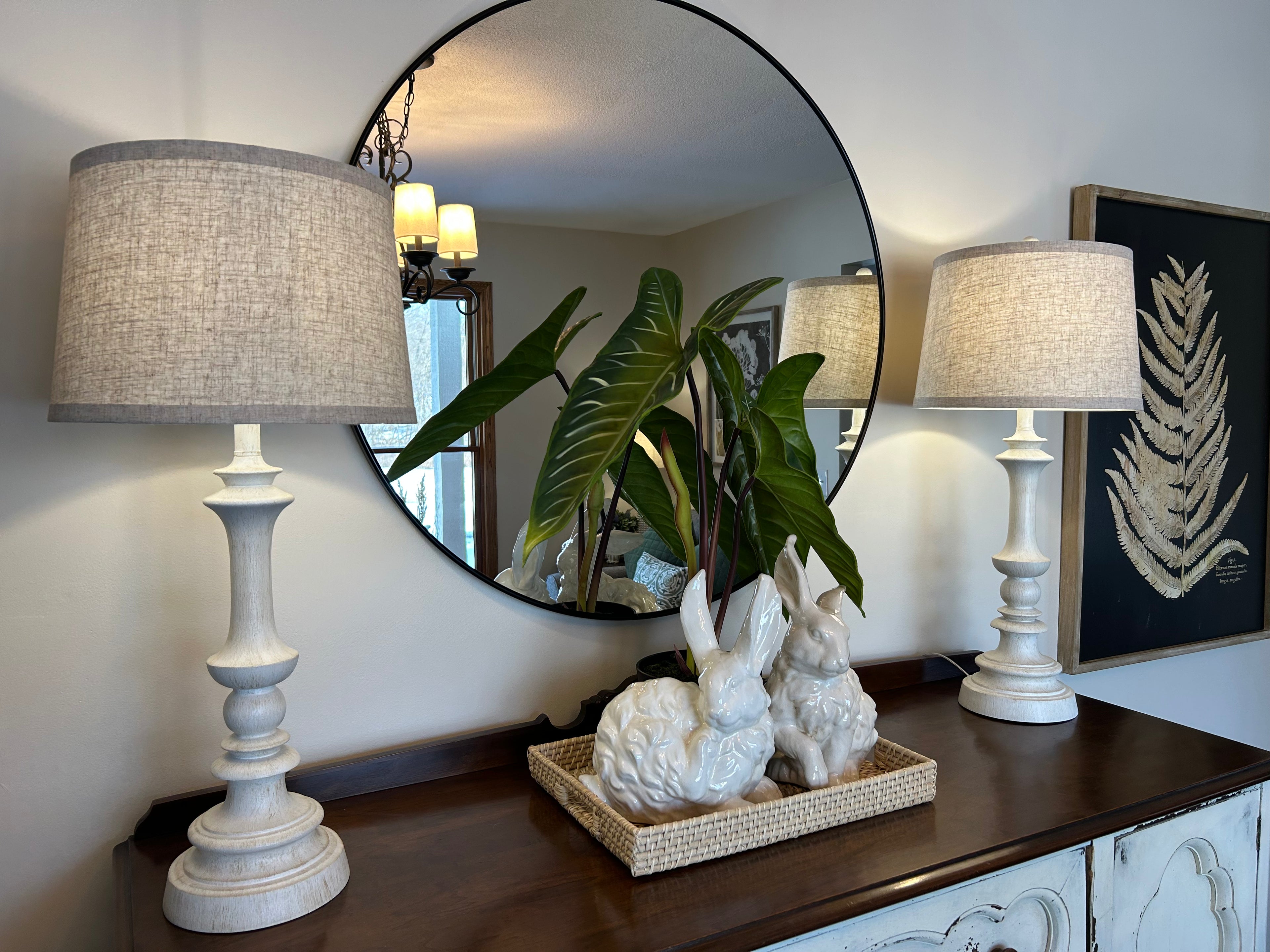 Decorative table with lamps, a mirror, and decorative items in a room setting.