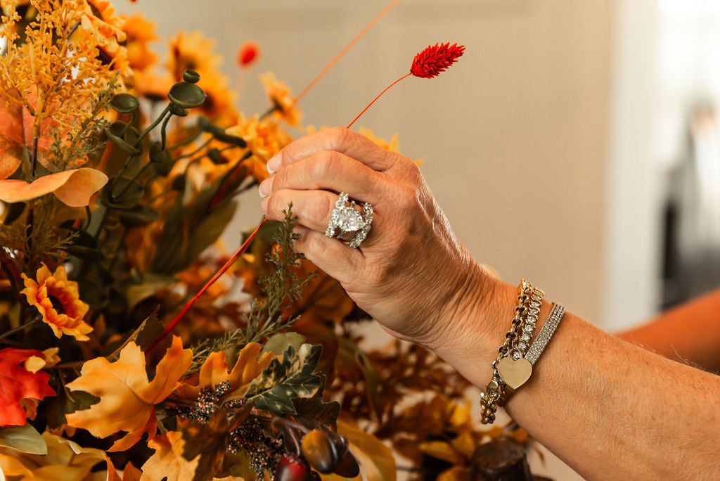 Hand with a ring and bracelet arranging flowers with a blurred background