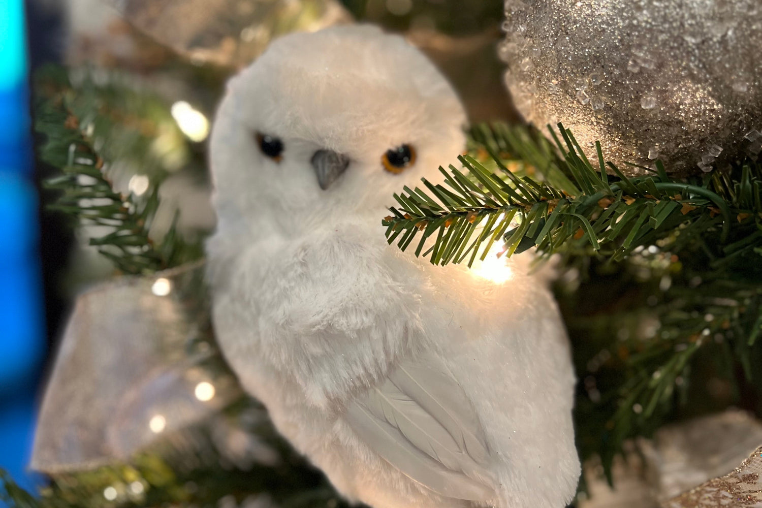 White owl figurine perched on a decorated Christmas tree with silver ornaments.