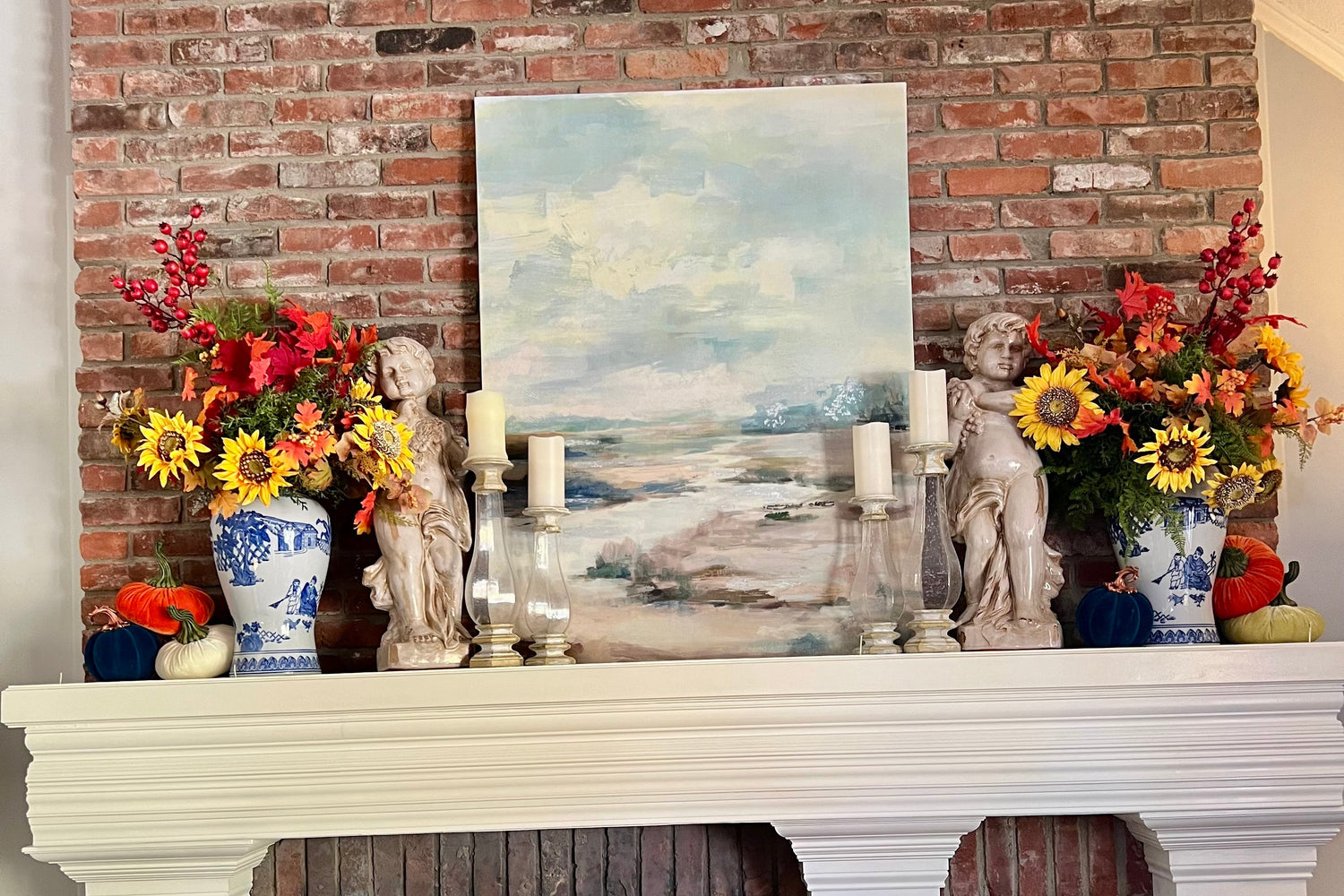 Decorative fireplace with a painting, statues, and flowers on a brick wall.