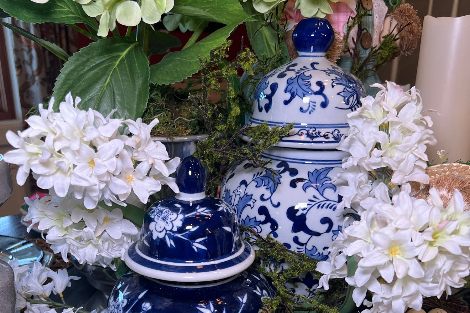 Decorative arrangement with blue and white ceramic vases, white flowers, green leaves, and a teddy bear.