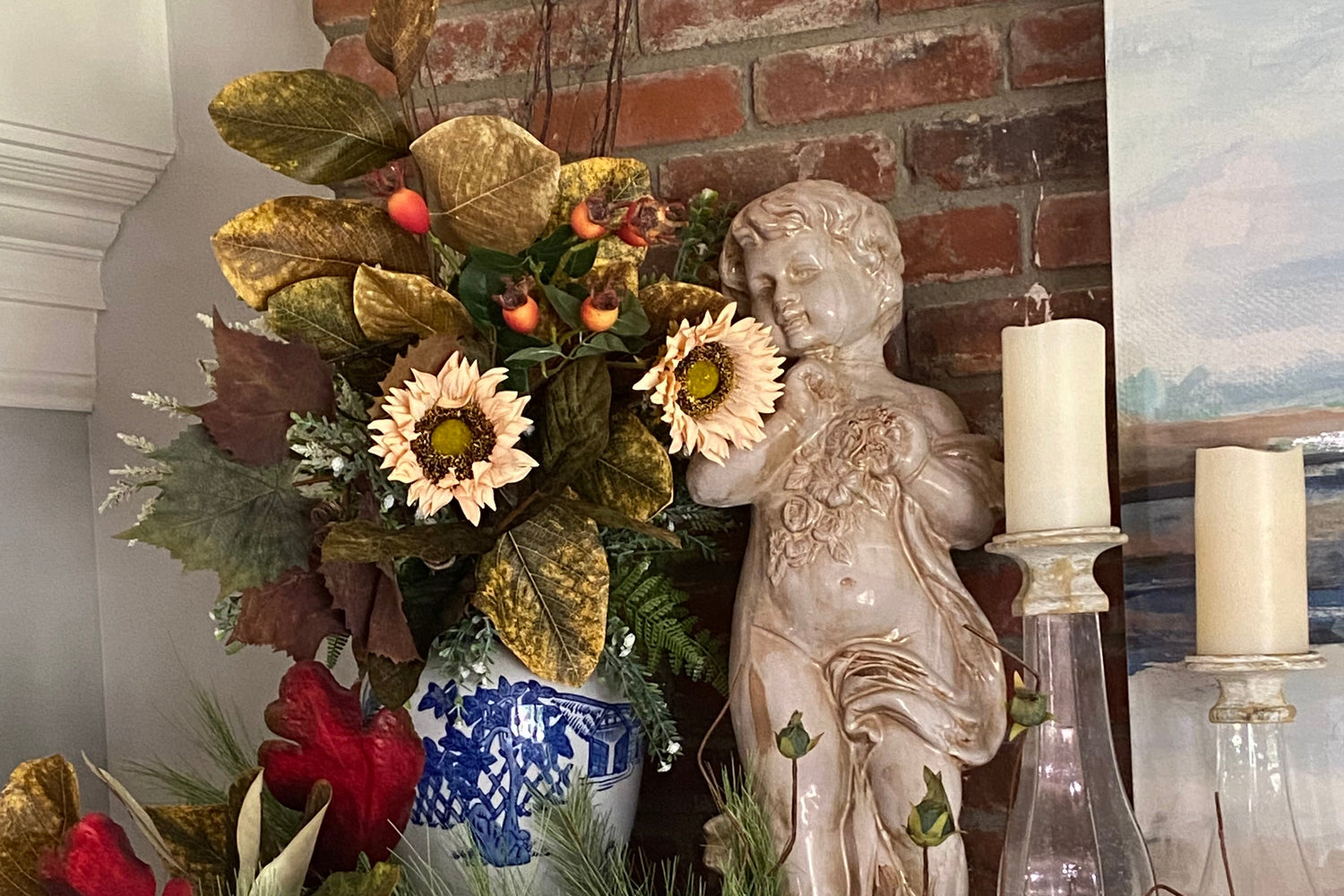 Decorative wreath with flowers, leaves, and a small angel figurine on a fireplace mantel.