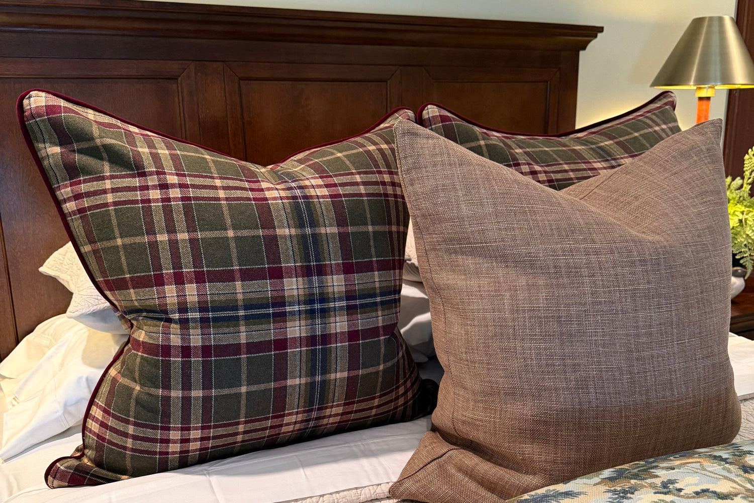 Plaid and solid-colored pillows on a bed with floral wallpaper.