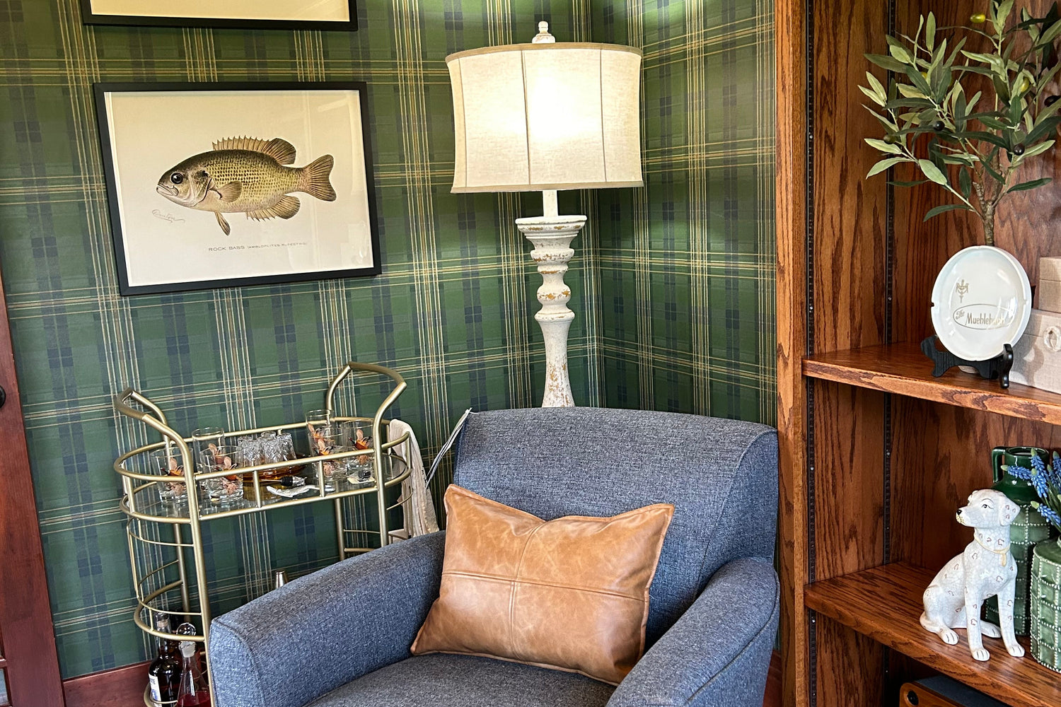 Denim chair in a plaid green and blue wallpaper with a fish picture and a standing lamp. 