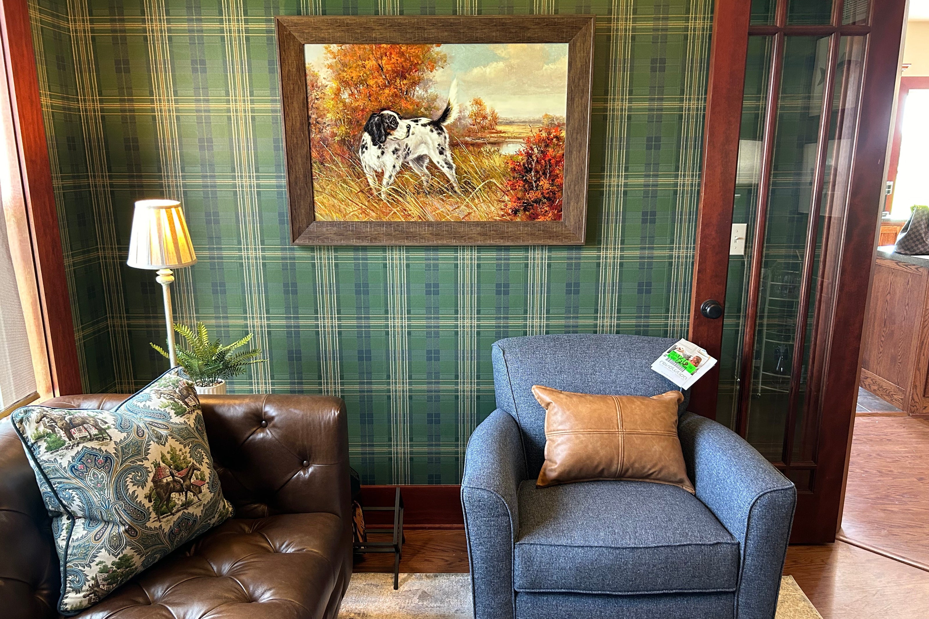 Green and blue plaid wallpapered room with a denim chair, rich dark chocolate tufted chesterfield sofa, and a classic hunting dog piece of artwork. 
