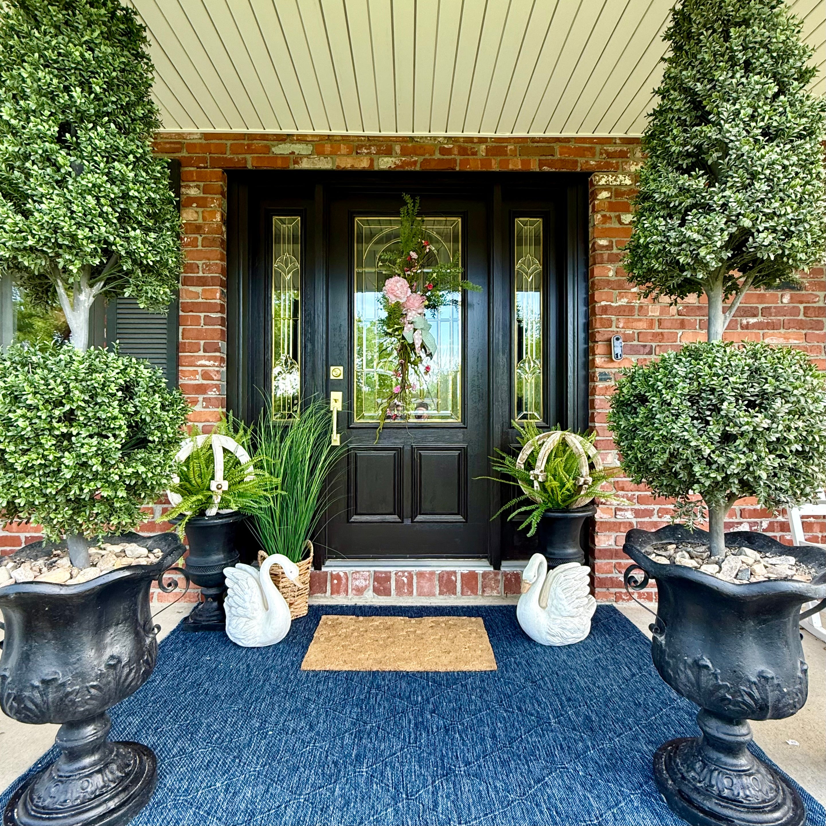 Front door of a house with decorative elements including urns, plants, and a doormat.
